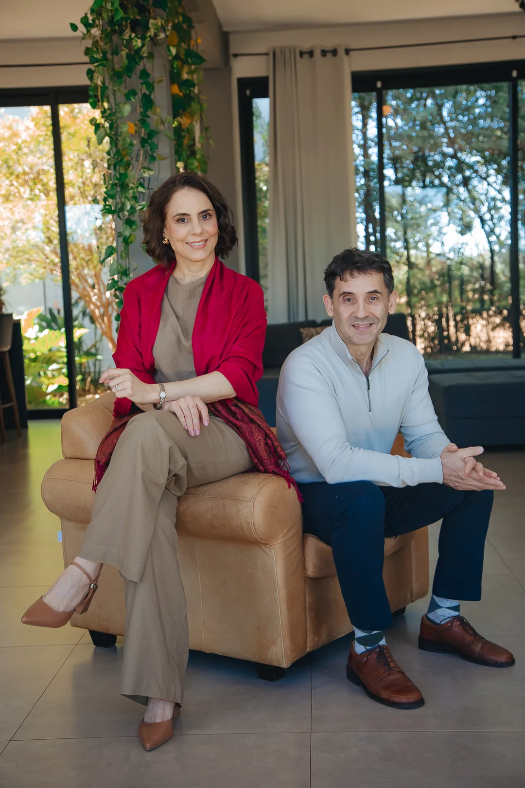 Sandra Caselato e Yuri Haasz sentados numa poltrona, em ambiente com plantas e luz natural